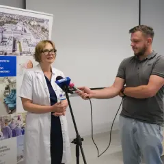 Lekarka w kitlu udziela wywiadu dziennikarzowi przed banerem Uniwersyteckiego Szpitala Klinicznego w Białymstoku.