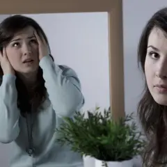 Kobieta w lustrze z przerażeniem zasłania uszy, odzwierciedlając niepokojące schizofrenia objawy.