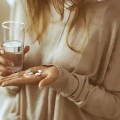Kobieta trzyma szklankę wody i kilka tabletek, w tym naproxen Hasco, gotowa do połknięcia.