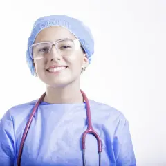 Uśmiechnięta lekarka w niebieskim fartuchu, czepku i okularach ochronnych ze stetoskopem.