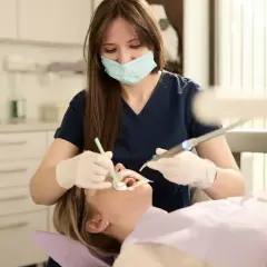 Dentystka w masce i rękawiczkach wykonuje zabieg stomatologiczny u pacjentki.