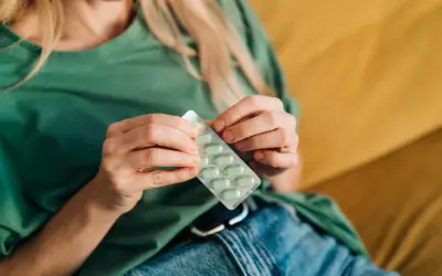Kobieta w zielonej bluzce trzyma opakowanie zielonych tabletek. Może to być lek na przeziębienie, suplement diety, albo coś na poprawę nastroju, jak np. vabinxo.