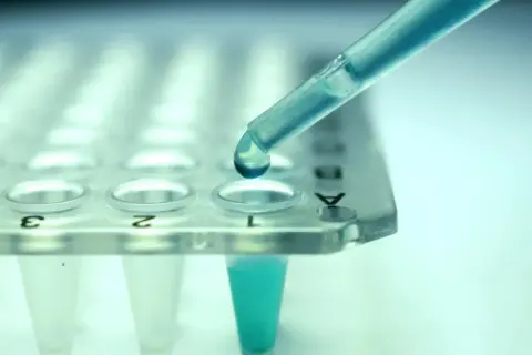 Kropla błękitnego płynu z pipety spada do probówki. To kluczowy etap w procesie leczenia biologicznego, gdzie precyzja jest najważniejsza.