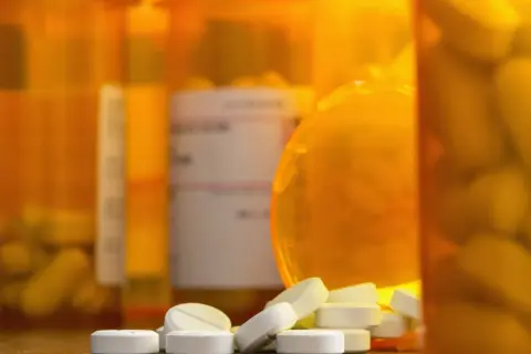 Białe tabletki rozsypane przed pomarańczowymi buteleczkami. Czy to oxycodone, co to za lek?