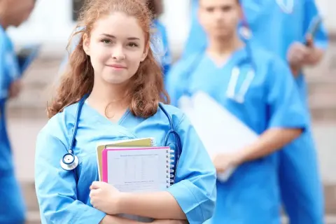 Młoda pielęgniarka w niebieskim uniformie z notatkami i stetoskopem, na tle innych medyków.