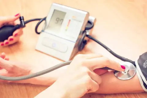 Dwie osoby mierzą ciśnienie. Jedna ręka trzyma pompkę, druga stetoskop. Na ekranie ciśnieniomierza widnieje wynik 97. To ważne, by kontrolować ciśnienie, zwłaszcza jeśli przyjmujesz leki, np. co Valsacor.