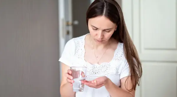 Kobieta trzyma szklankę wody i tabletkę na dłoni.
