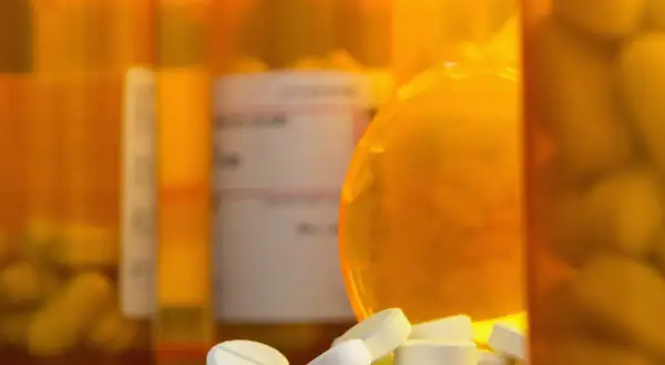 Białe tabletki rozsypane przed pomarańczowymi buteleczkami. Czy to oxycodone, co to za lek?