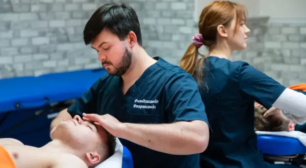 Fizjoterapeuta wykonuje masaż twarzy pacjentowi, w tle druga fizjoterapeutka.