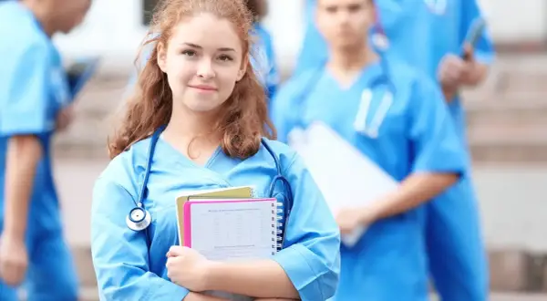 Młoda pielęgniarka w niebieskim uniformie z notatkami i stetoskopem, na tle innych medyków.