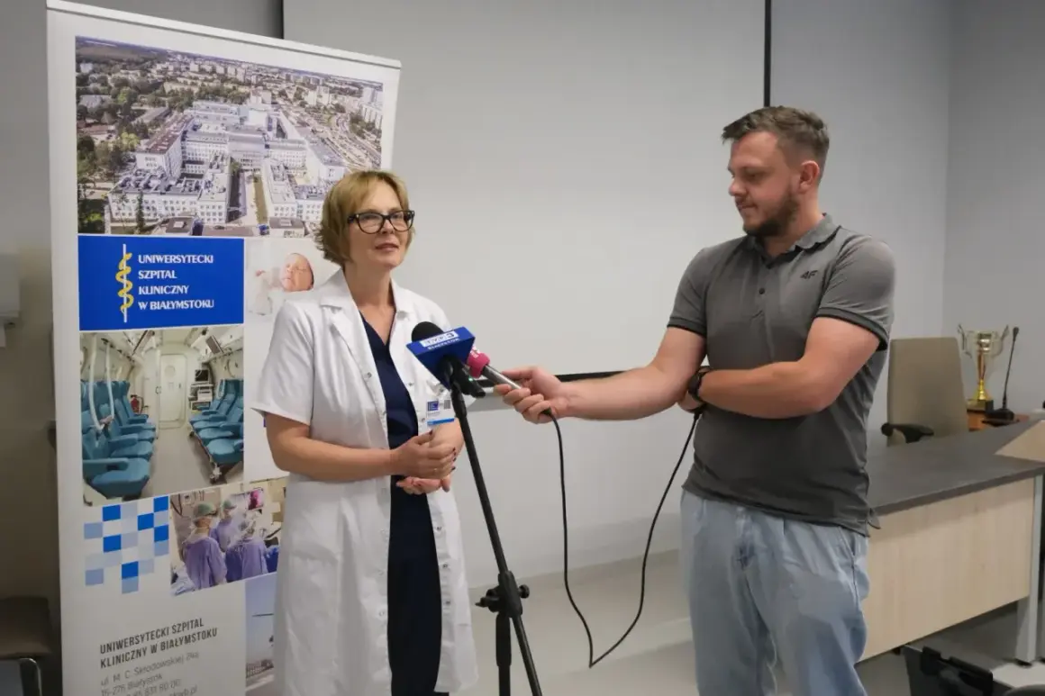 Lekarka w kitlu udziela wywiadu dziennikarzowi przed banerem Uniwersyteckiego Szpitala Klinicznego w Białymstoku.