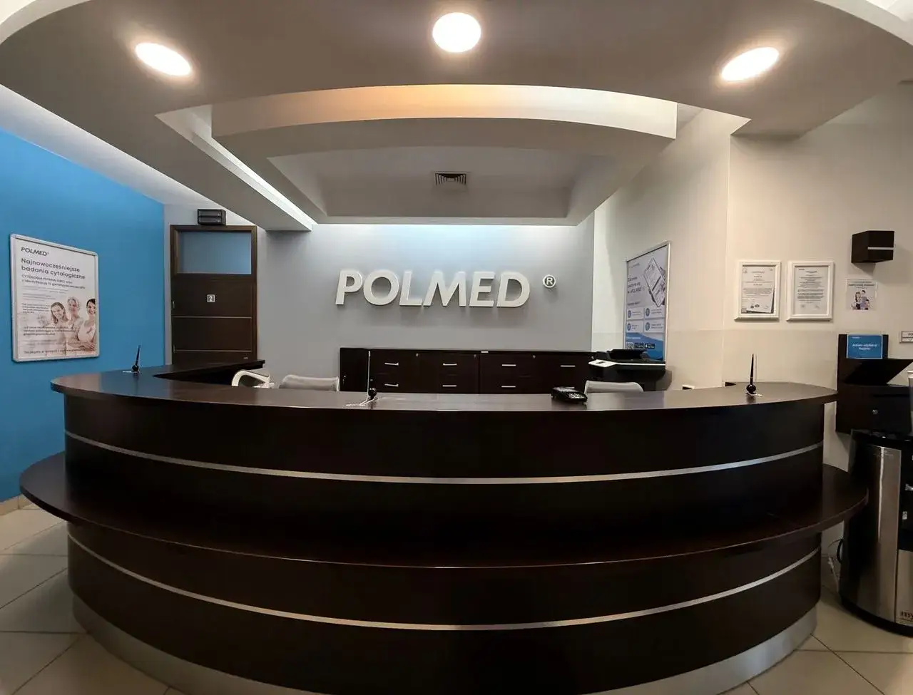 Recepcja kliniki medycznej Polmed z ciemnobrązowym ladą i logo na ścianie.