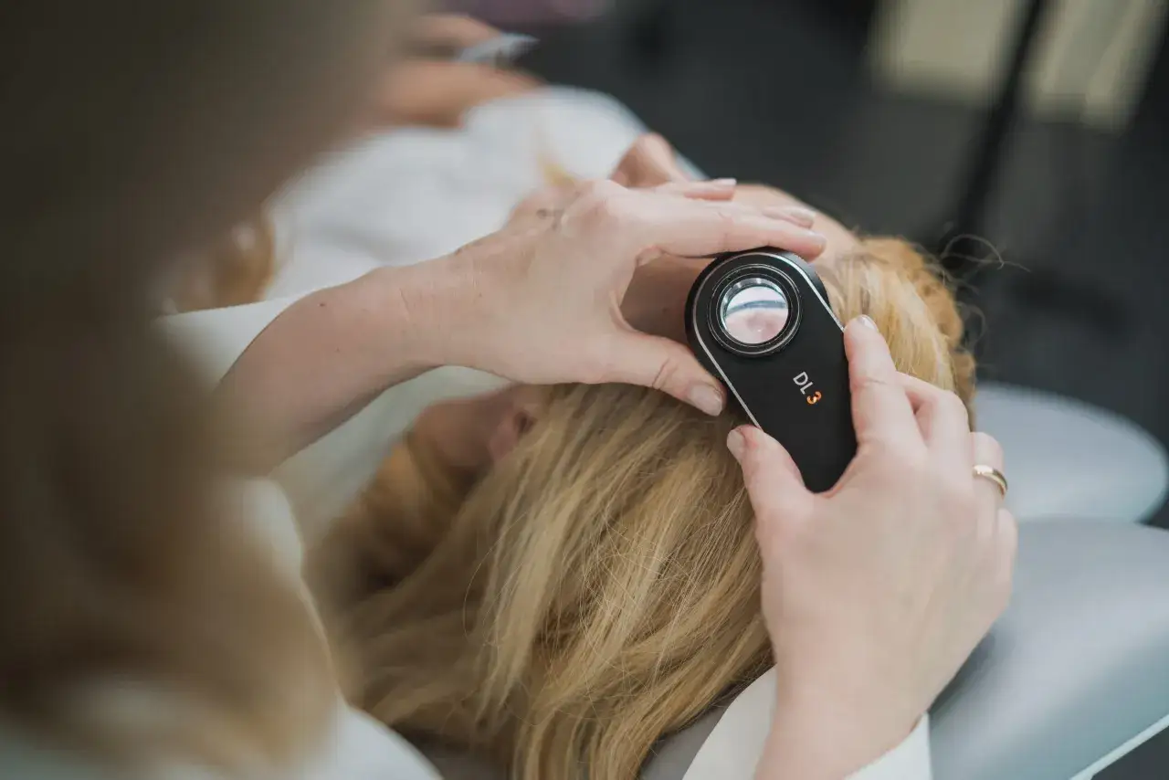 Dermatolog bada skórę głowy pacjentki za pomocą dermatoskopu.