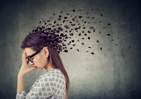 Kobieta z ręką na czole, której głowa rozpada się na kawałki. Symbolizuje to trudności z koncentracją i przebodźcowaniem, często występujące jako adhd u kobiet objawy.