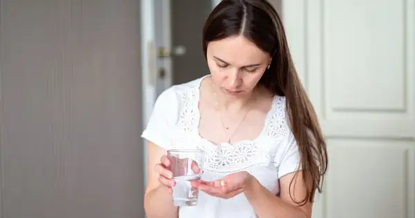 Kobieta trzyma szklankę wody i tabletkę na dłoni.